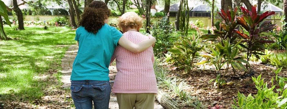 Granddaughter helping her disabled grandmother walk with the aid of a walker.