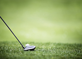 Golf ball behind driver at driving range, plenty of copy-space and very shallow depth of field.