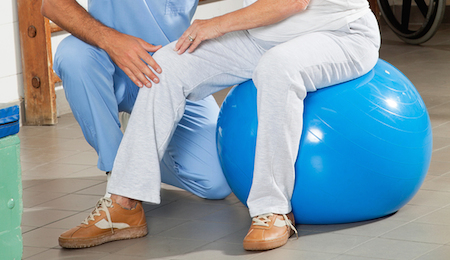 Young physical therapist examining senior woman's knee at hospital gym