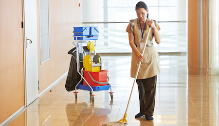 Female cleaner maid woman worker with mop in uniform cleaning corridor pass or hall floor of busines