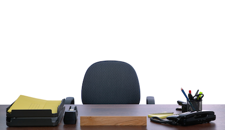 Desk with nobody sat at it against a white background. Blank name sign to add your own text.