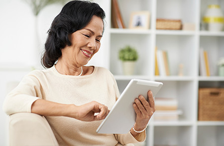 Smiling Woman is Seated Using a Tablet Device 